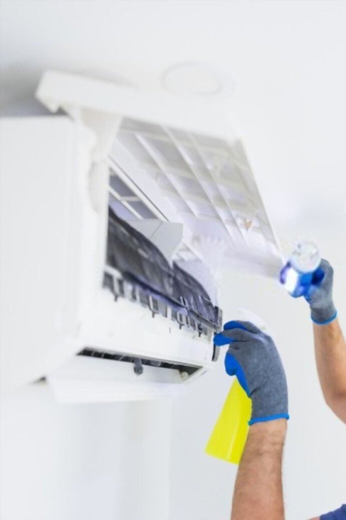 Technician cleaning wall-mounted split AC with spray and flashlight