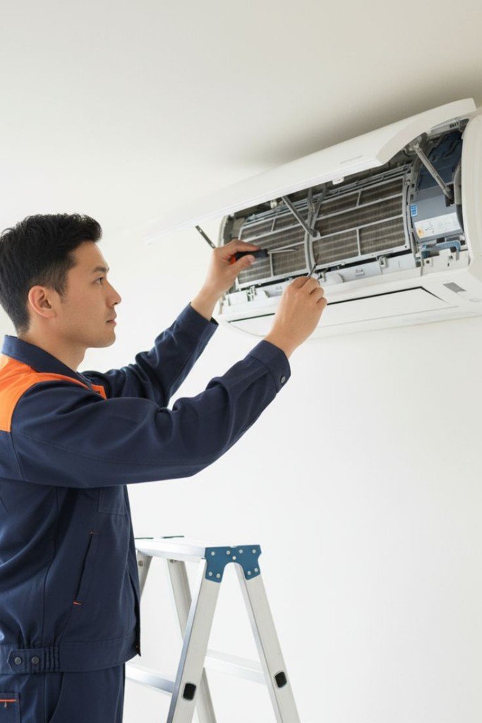 Technician on ladder repairing split AC indoor unit